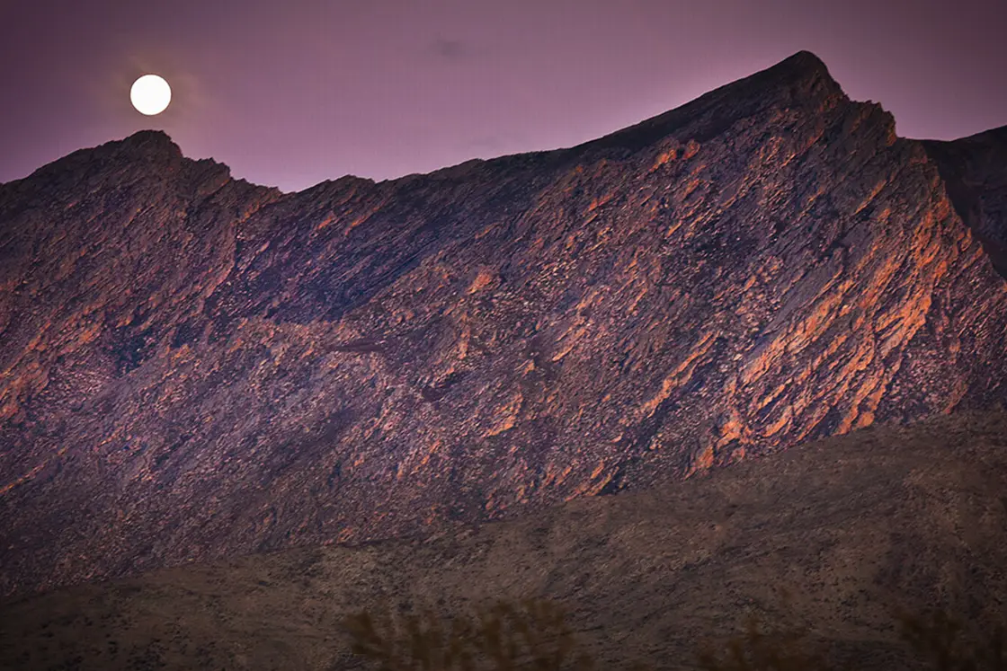 Perfect Hideaways property for sale: A sunset photograph of the dramatic mountains, typically found in the Karoo, with the moon rising above a mountain peak. Olive Farm in Prince Albert.