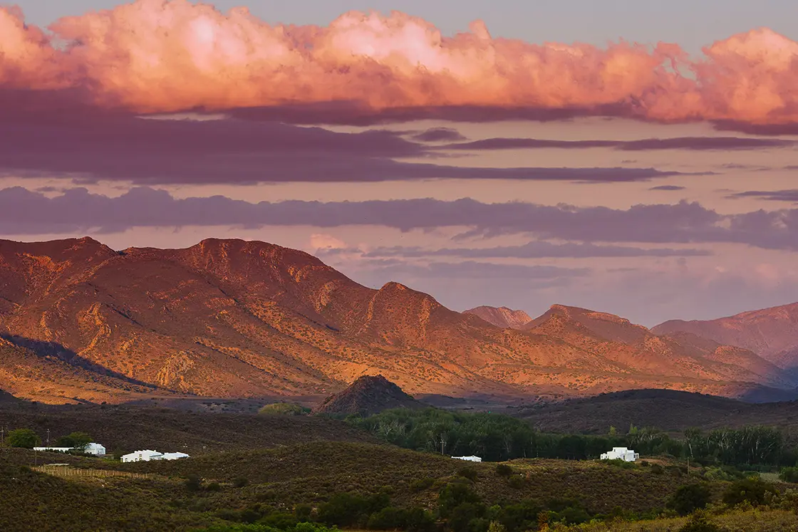 Perfect Hideaways property for sale: A view of the farm during sunset, featuring the sloping mountains and hills of the Karoo. Olive Farm in Prince Albert.