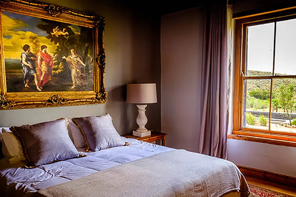 Perfect Hideaways property for sale: A bedroom area with a double bed, the room features rich colours visible in the painting which hangs above the bed, and in the luxurious bedding. Olive Farm in Prince Albert.