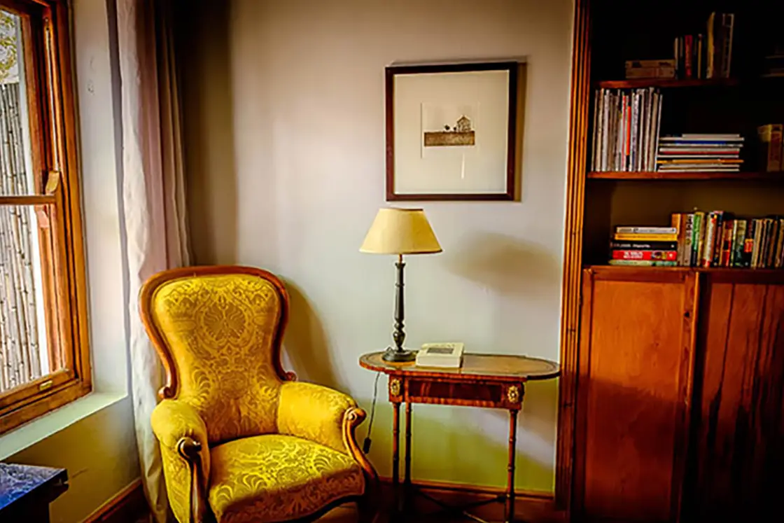 Perfect Hideaways property for sale: An antique yellow-gold chair stands in the corner of a bedroom, wooden furnishings, and heritage elements visible in the home’s architecture. Olive Farm in Prince Albert.