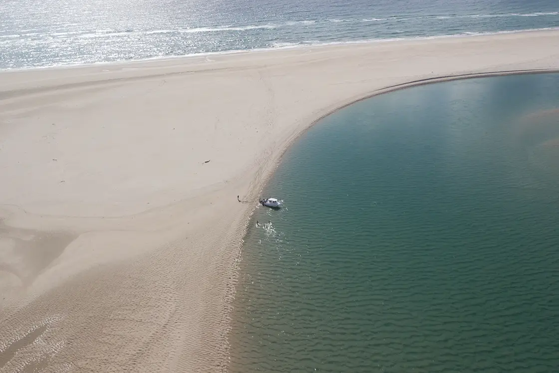 Perfect Hideaways real estate property: A flat sand bank bordered by the open ocean on one side, and a small waterway with a boat on the other side. The Sanctuary Private Reserve, Mozambique.