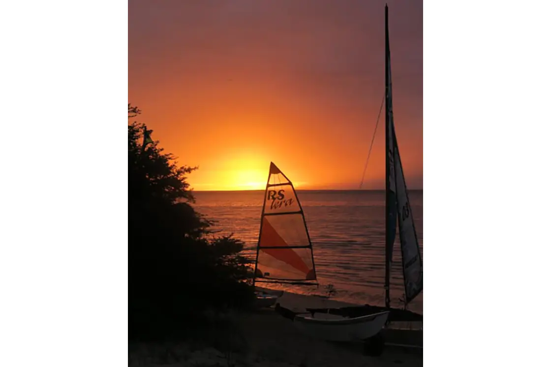 Perfect Hideaways real estate property: A silhouette of the sail of a boat on a beach, featuring a pink and orange sunset on the horizon. The Sanctuary Private Reserve, Mozambique.