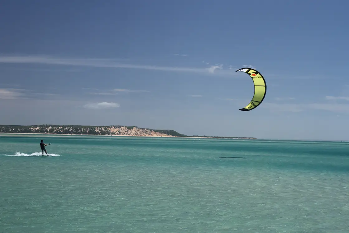 Perfect Hideaways real estate property: A kite surfer riding in shallow blue water, with a yellow kite, and the Mozambican coastline in the background. The Sanctuary Private Reserve, Mozambique.