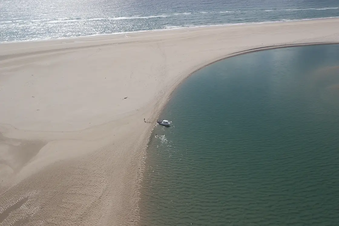 Perfect Hideaways real estate property: A flat sand bank bordered by the open ocean on one side, and a small waterway with a boat on the other side. The Sanctuary Private Reserve, Mozambique.