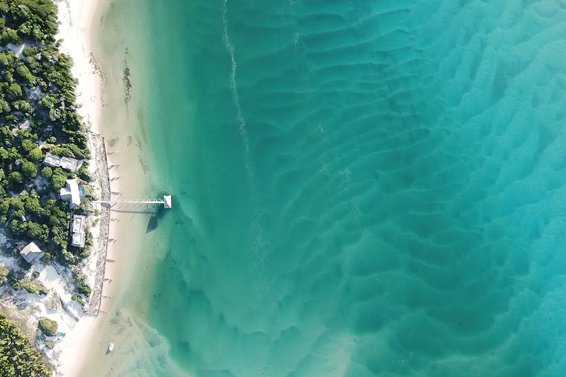 Perfect Hideaways real estate property: An aerial photograph of the clear blue shallow water beside a plot of land, featuring a dock for water access, and low-impact guest lodging. The Sanctuary Private Reserve, Mozambique.