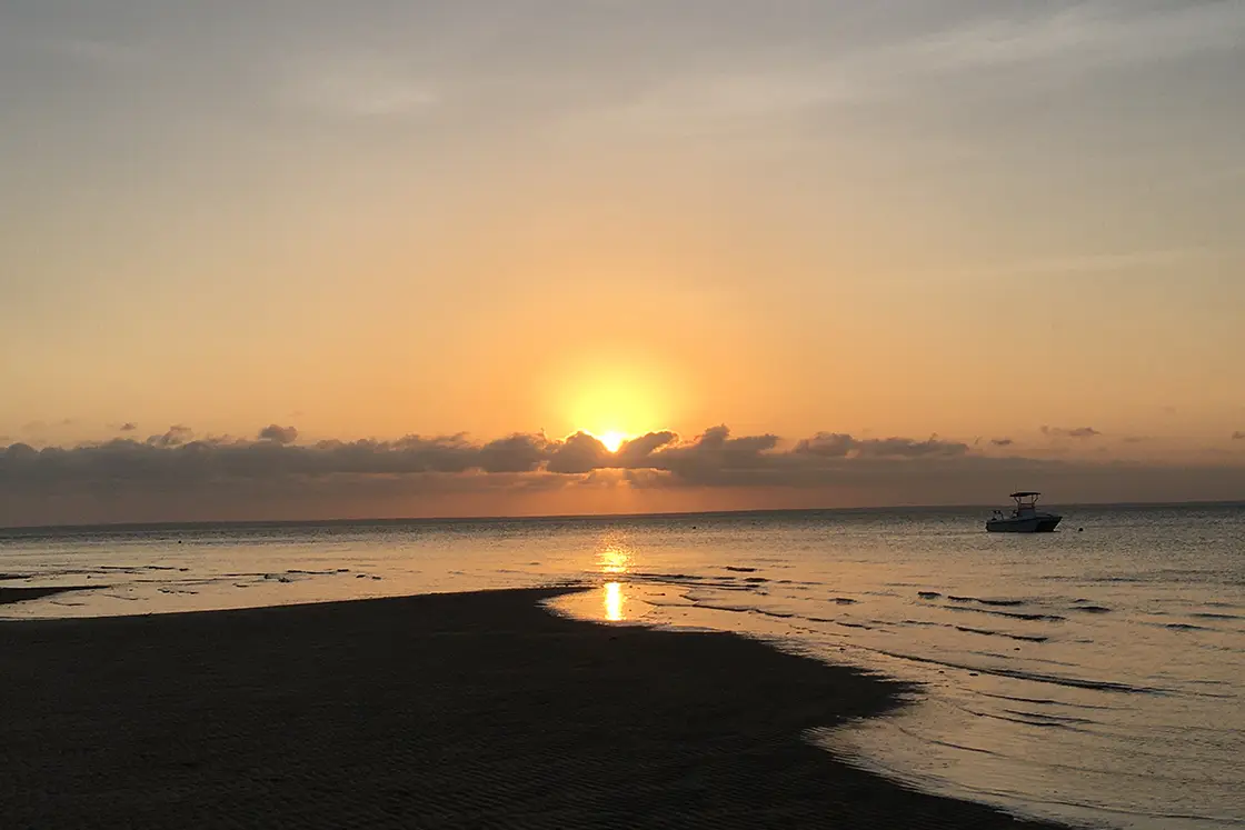 Perfect Hideaways real estate property: Lapping water on a beach during sunset, with a boat anchored nearby. The Sanctuary Private Reserve, Mozambique.