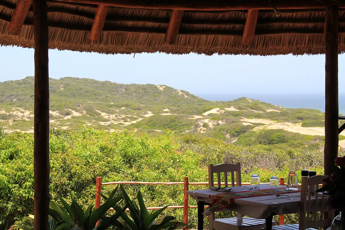 Perfect Hideaways real estate property: A dining table set up with the dunes and bush and the sea in the background. Dunes de Dovela Lodge, Mozambique.