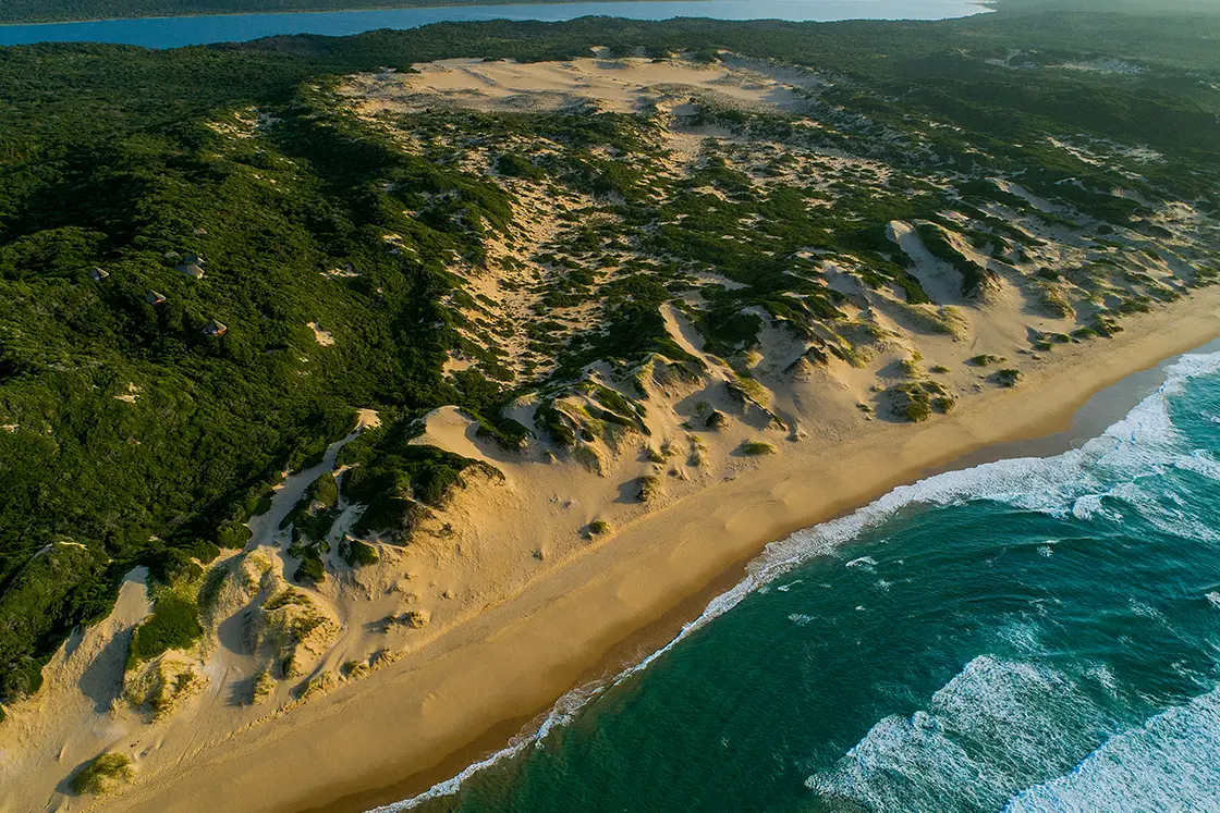 Perfect Hideaways real estate property: An aerial view of the beach and the lagoon at a distance. From the beach looking out towards the dunes and over a bank of Verbena. Dunes de Dovela Lodge, Mozambique.