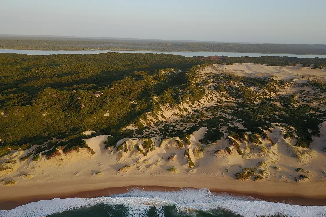 Perfect Hideaways real estate property: The beach at a bird's eye view with the sun setting on the sand dunes and the lodges plotted within the surroundings. Dunes de Dovela Lodge, Mozambique.