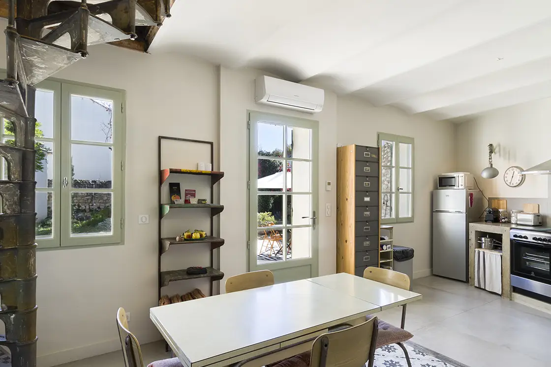 Perfect Hideaways property for sale: A well-lit living space inside the French villa, which features shutter green window panes and a spiral staircase beside the dining table. France, Villa Sancti.