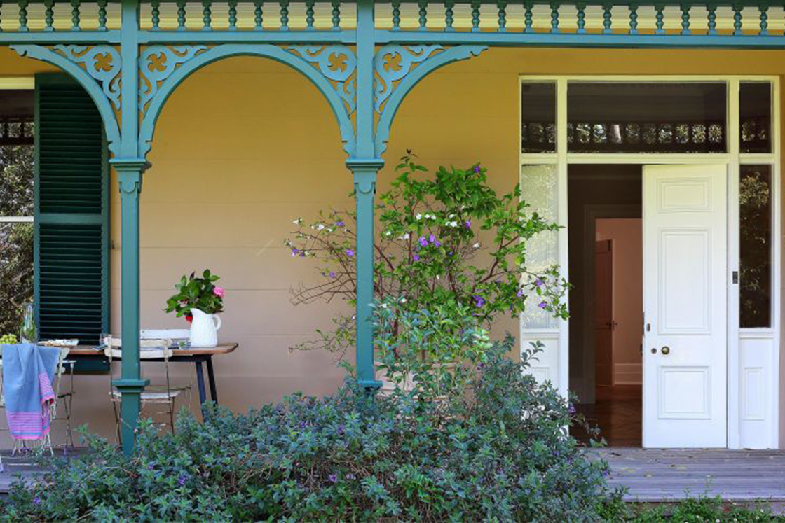 A wrap-around porch with outdoor dining area, the porch features wrought iron fretwork arches which complement the heritage home's emerald shutters.