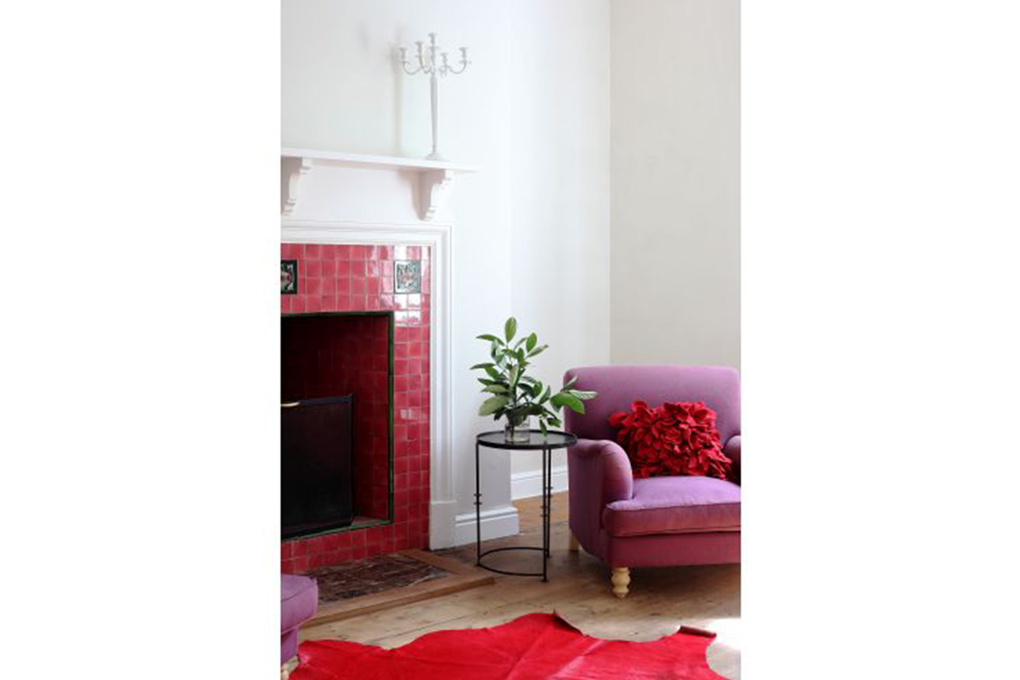 Mantel shelf with candelabra and decorative Victorian corbel above ruby tiled indoor fireplace. Decor reflects the reddish tones of the fireplace.