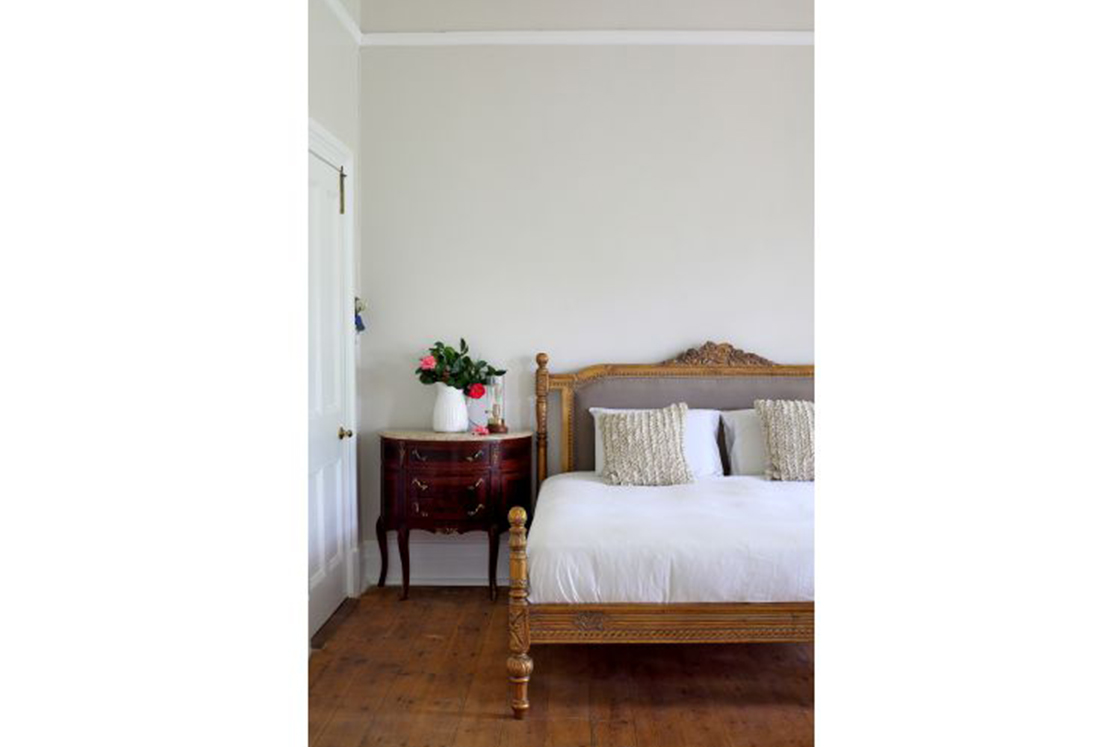 Bedroom featuring Oregon pine floor and complementary bed frame, ornate dark-wood side table.