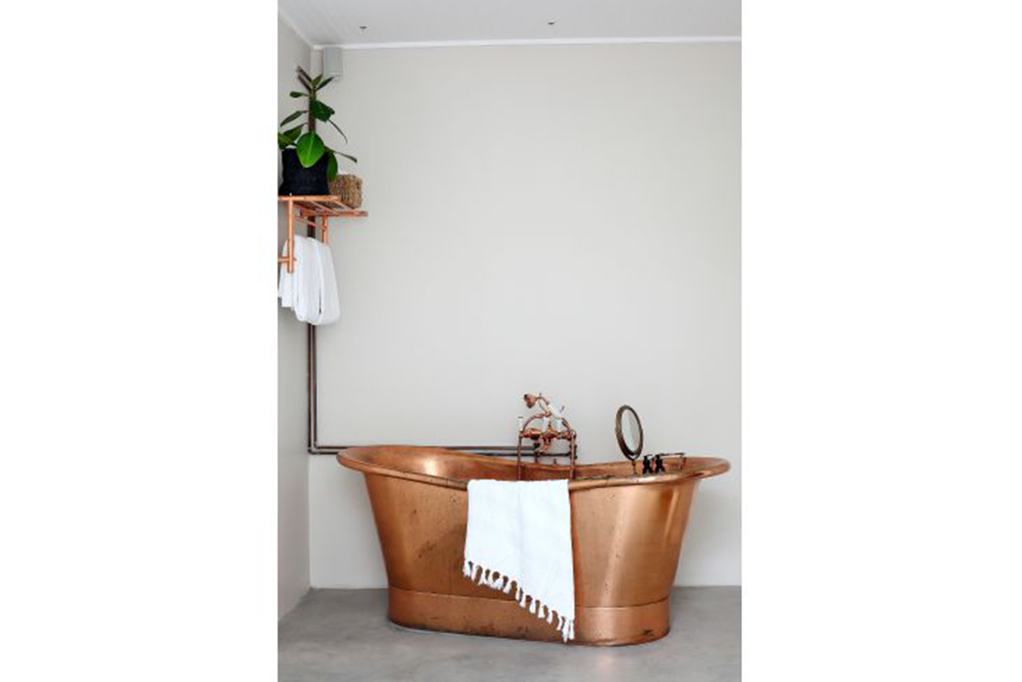 En-suite bathroom featuring copper finishes seen in the bathtub and towel rack.