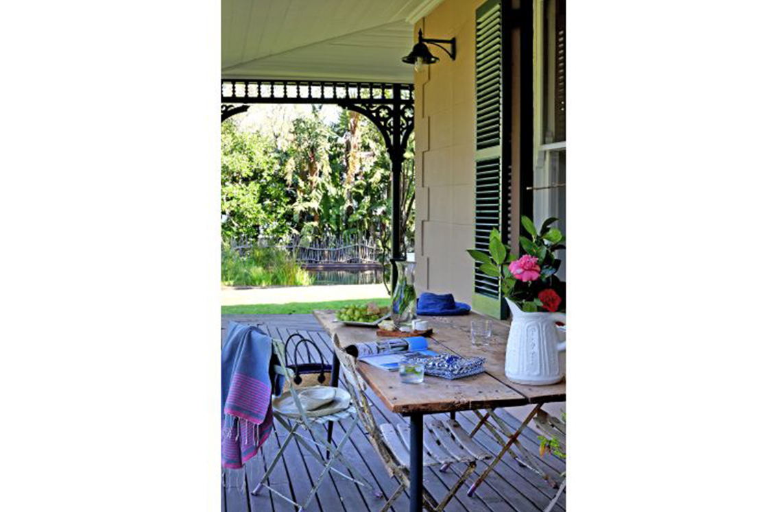 Outdoor dining area complete with charcuterie board and flowers. Charming overhead lighting, wrought iron arches, and emerald shutters complete this idyllic lunch setting.