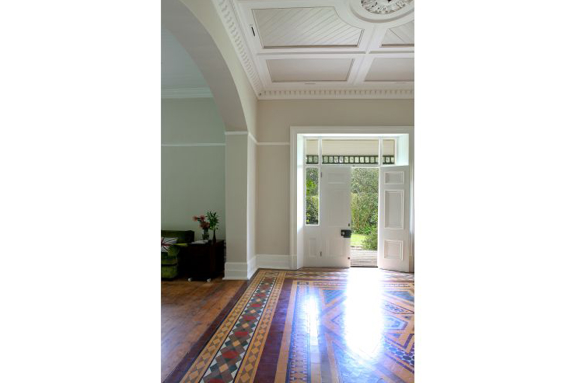 Spacious entrance hall with minimal decor showcasing the home's Victorian character through simple arches, intricate floor pattern, ceiling rose and detail.