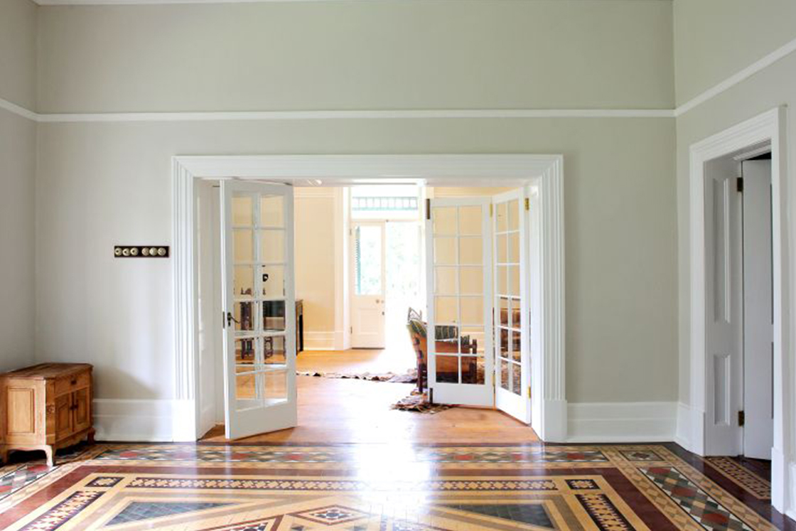 Minimally decorated Victorian entrance hall with marquetry style elements reflected in the floor. Double cottage pane tri-fold doors with industrial light switches.