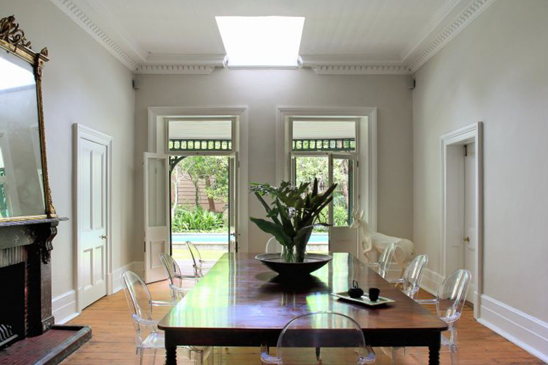 Dining area with Victorian character and neutral tones contrasted by a dark wood table, indoor fireplace and wood floor. Skylight.