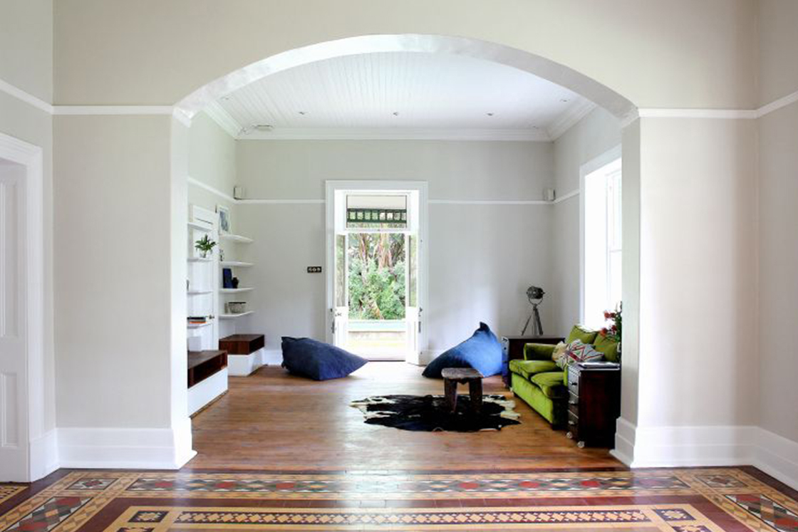 Spacious living area featuring minimalist decor. Dark tones in the furniture contrast the neutral tones in the home's Victorian architecture.