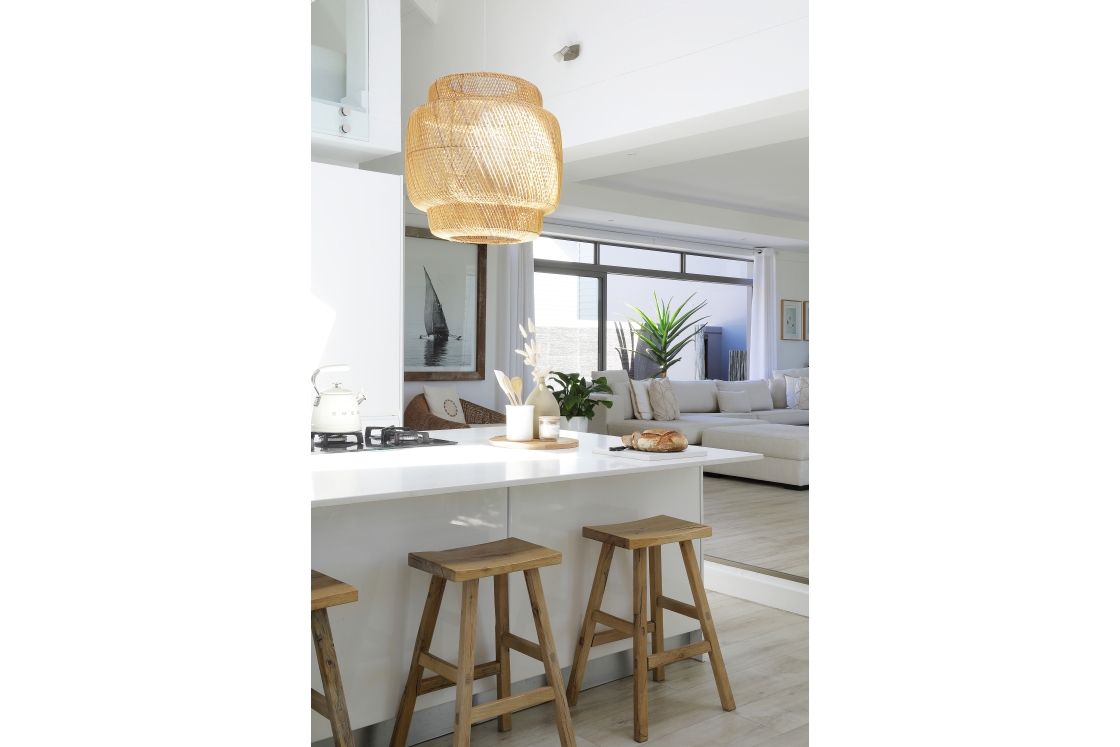 The marble kitchen counter top with white cabinets, wooden stools and a large hessian chandelier.