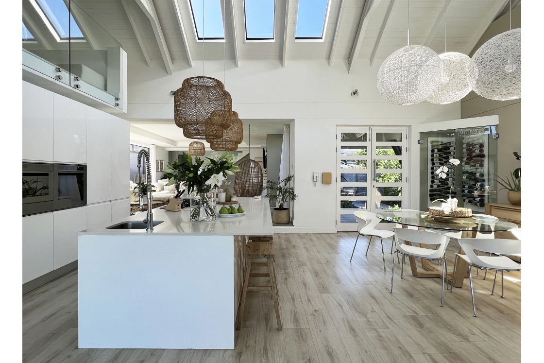 A well-lit kitchen with a skylight, featuring polished wooden floors and the open-plan dining room table with white chairs.