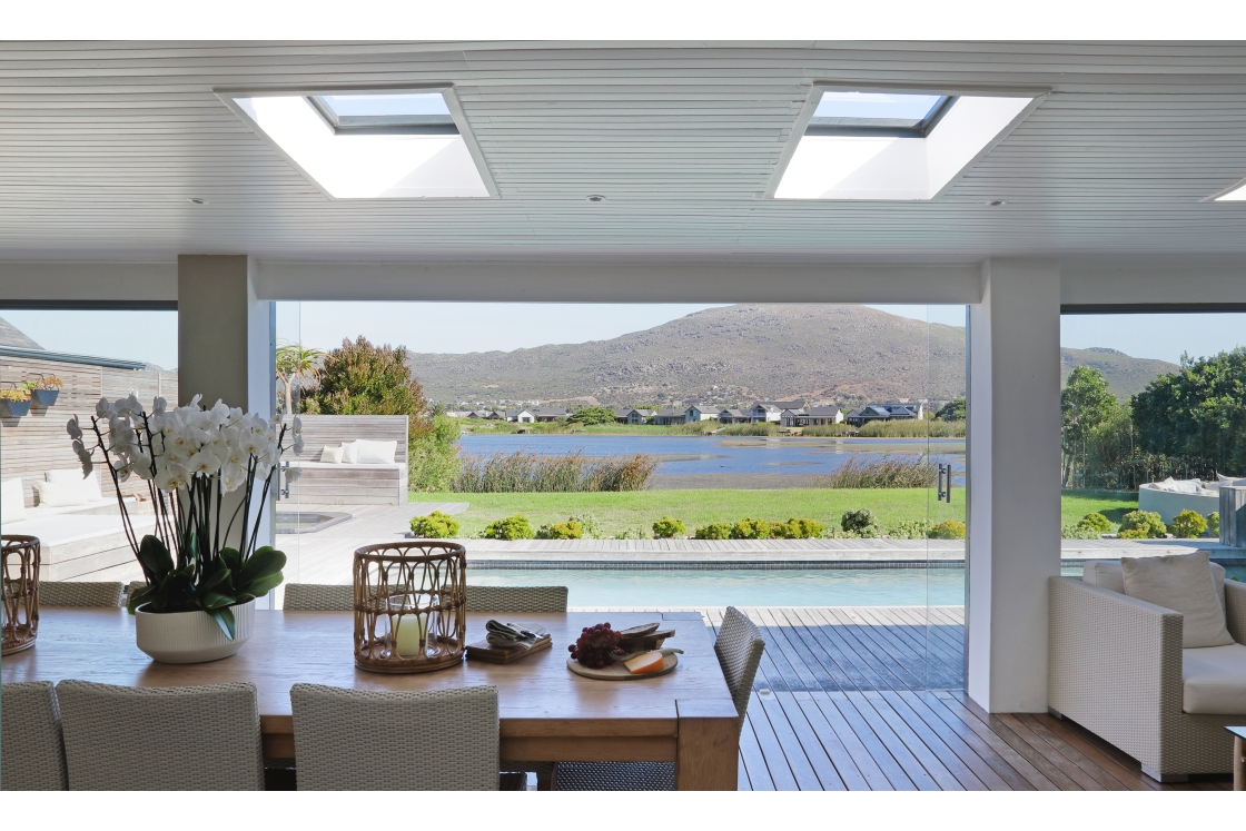 A stylish living room with expansive windows and sky lights offering a view of the pool, lawn and lake.