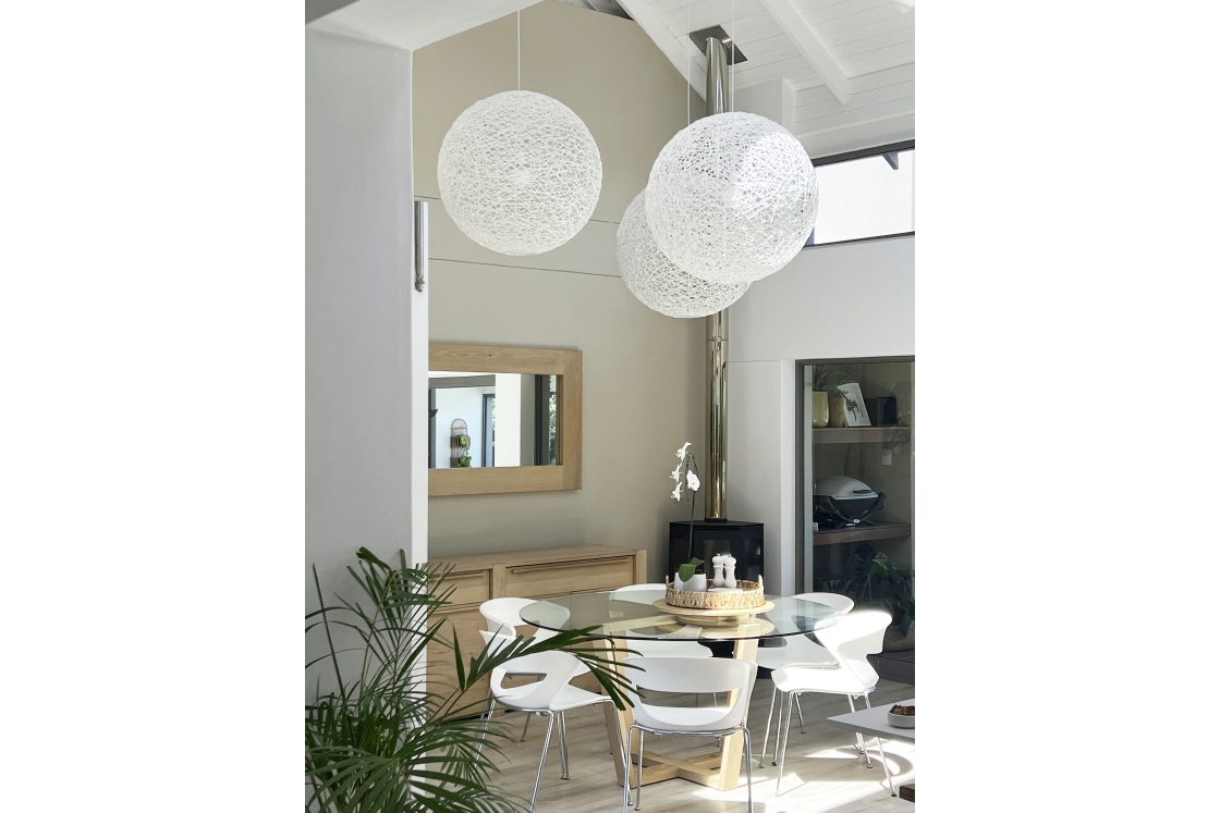 A modern dining room with white chairs and a prominent white pendant light.