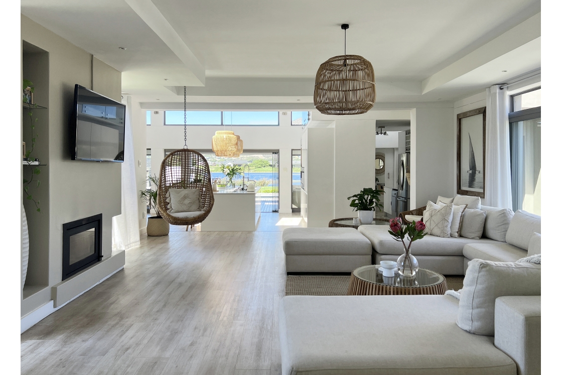 A contemporary living room featuring white couch and elegant wooden floors, open-plan kitchen.