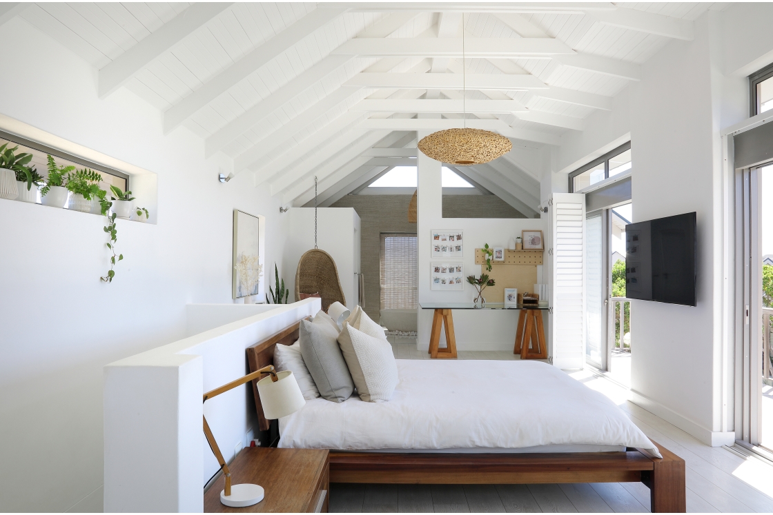 A minimalist bedroom with clean white walls and wooden floors, white wooden ceilings and a private balcony.