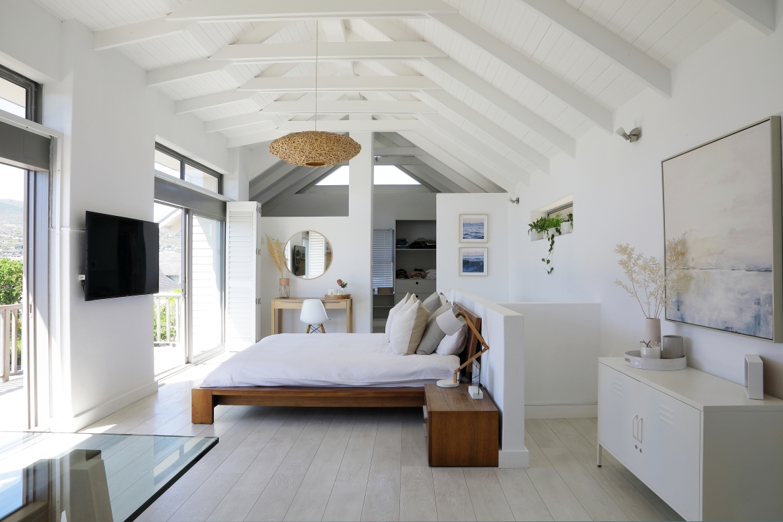 A minimalist and elegant bedroom showcasing white walls and wooden floors, and white wooden high ceilings.