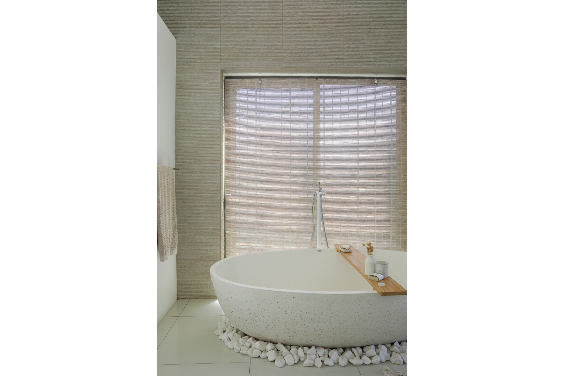 A white bathtub occupies the center of a bathroom, with a window providing light and a view of the outside.