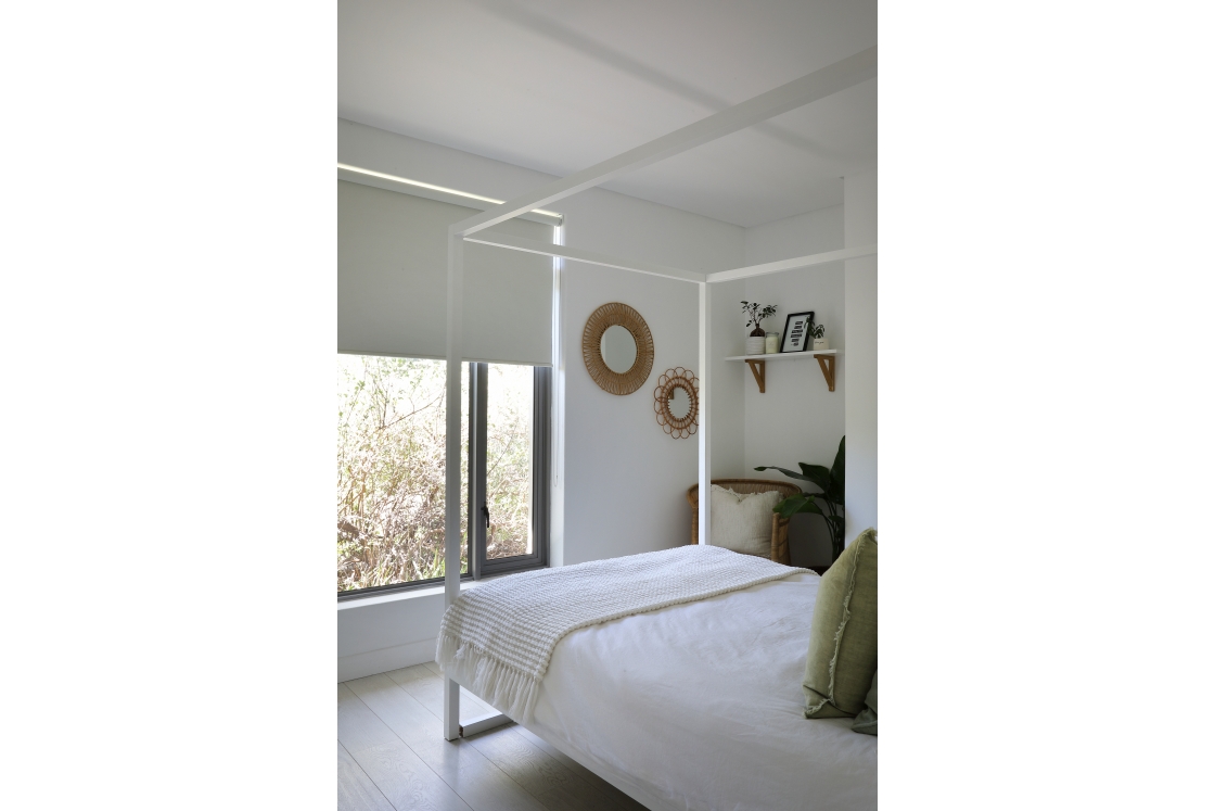 Angled photo of a white bedroom with showcasing a canopy bed and hessian decor and a window.