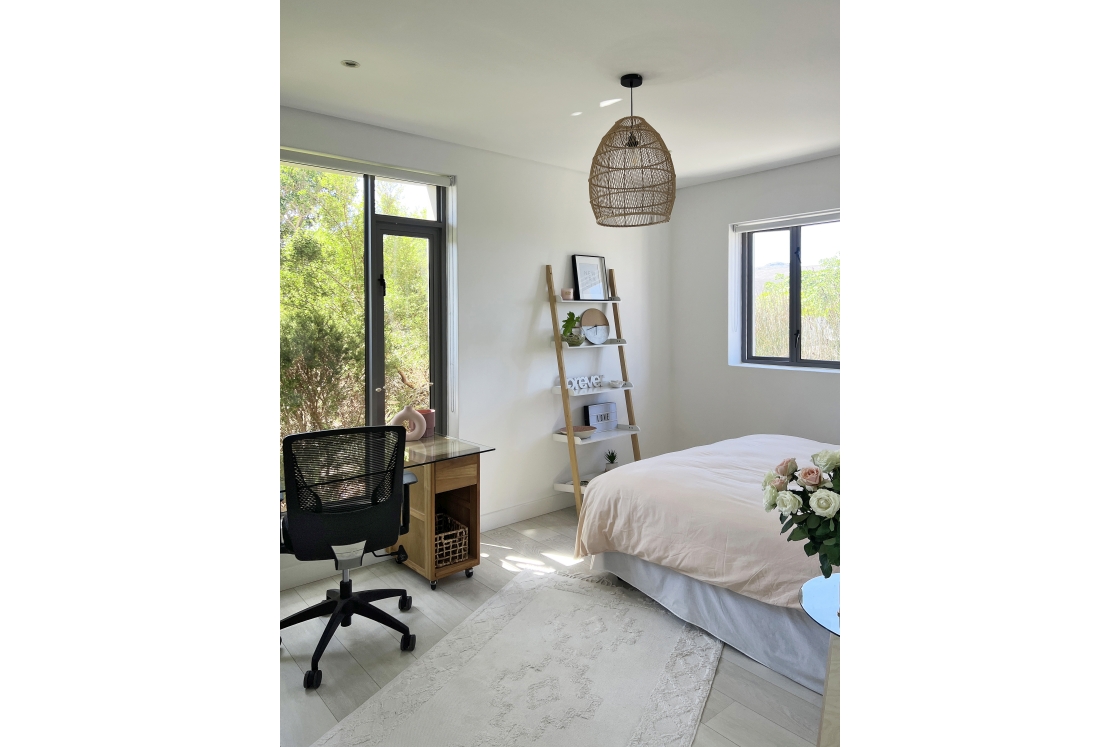 A cozy bedroom captured from an angle, showcasing a bed with a pink bed covers, desk and chair, and a window.