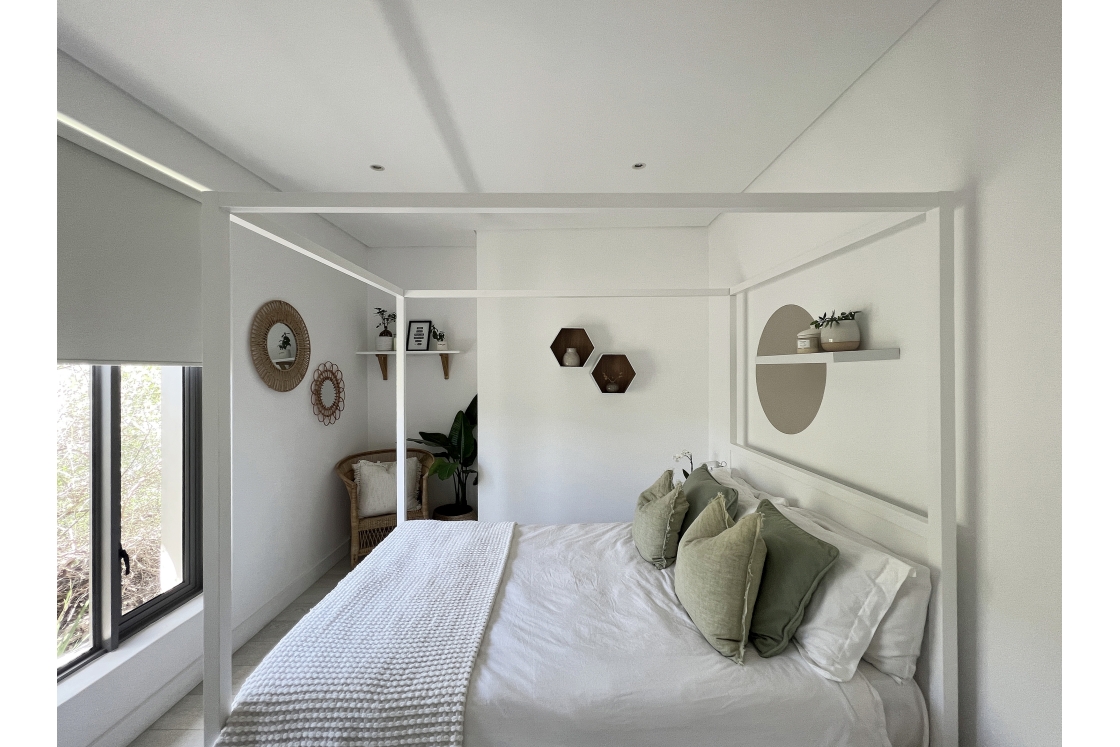 A bright white bedroom showcasing a canopy bed and a window.