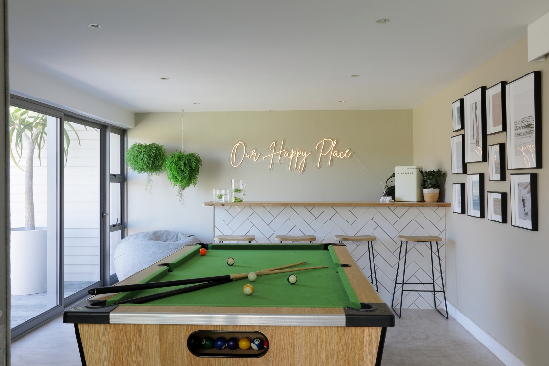 A pool table positioned in a room featuring a wall of plants and a bar.