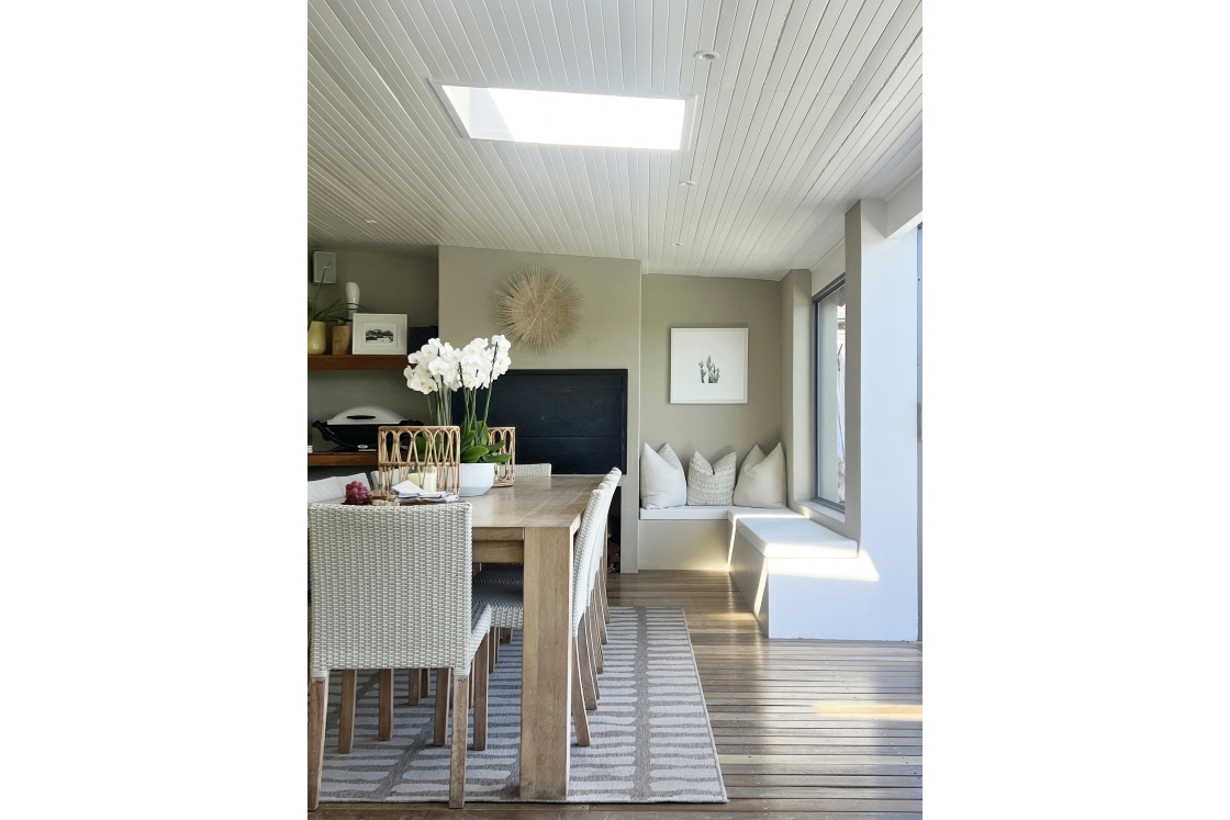 A dining room featuring a wooden table surrounded by chairs with barbecue area and white wooden ceilings and sky lights.