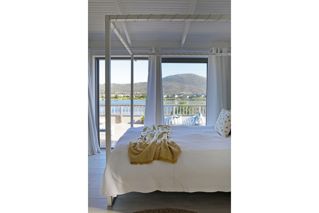 A serene bedroom featuring large windows that offers a view of the water and balcony.