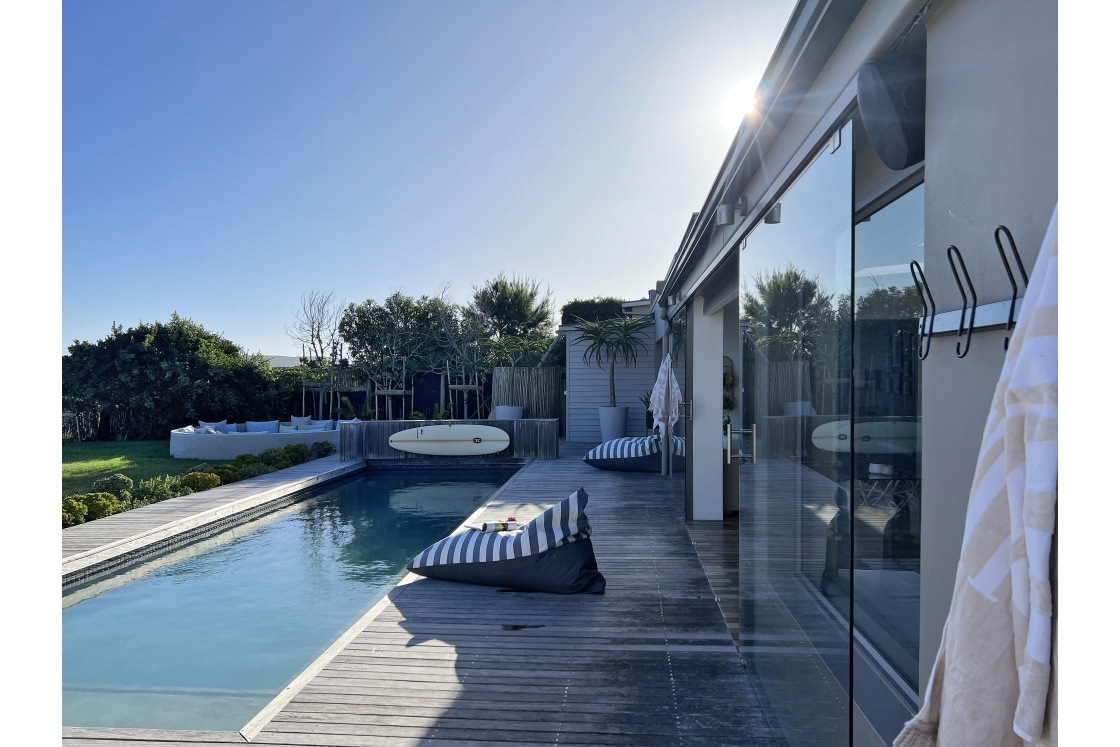 A pool area showcasing a pool pillow, a surf board rack, and the indoor-outdoor entertaining area.