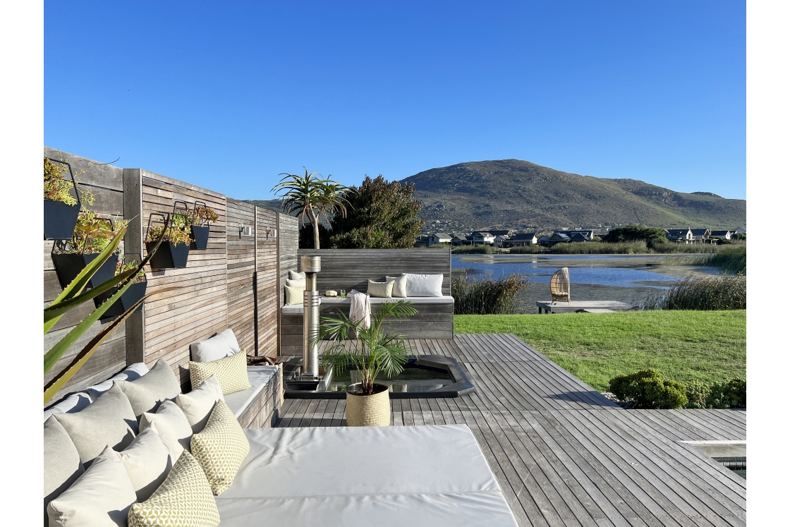 A wooden deck equipped with a soft couch and jacuzzi, presenting a beautiful view of the lake.