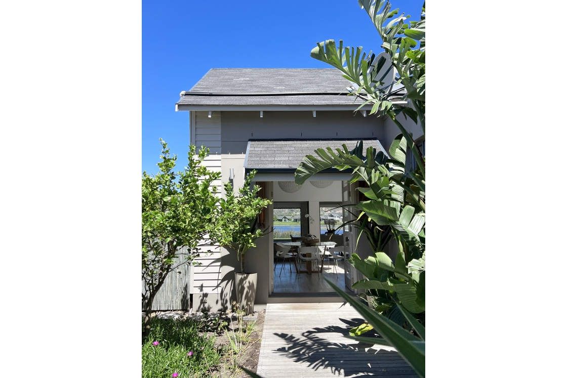 A charming house featuring a wooden walkway leading to a vibrant garden filled with various plants.