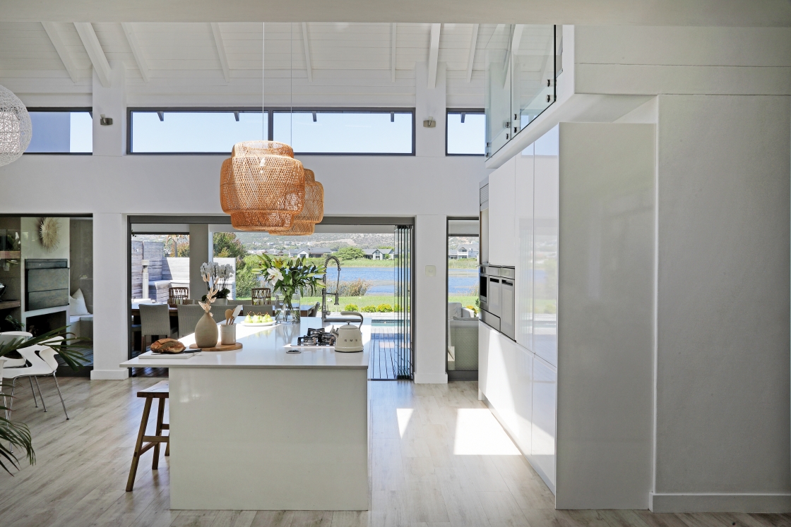 A modern kitchen featuring a spacious island and a large window overlooking the outdoor entertaining area and lake view.