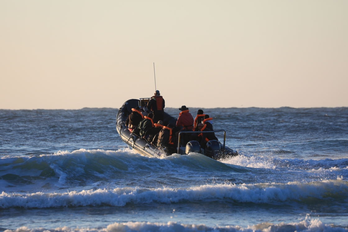 An image depicting choppy water with a boat being launched out to sea with people onboard in lifejackets.