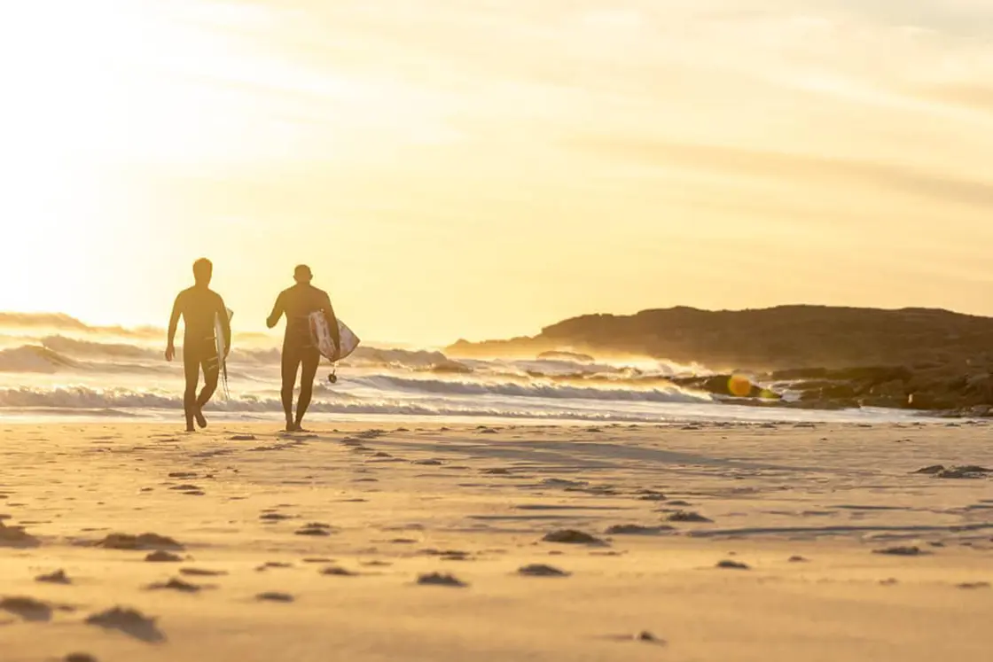 Perfect Hideaways property for sale: Two surfers walking home along the beach, near a plot of land for sale, as the ocean is bathed in sunset colours. Trekoskraal, Paternoster.