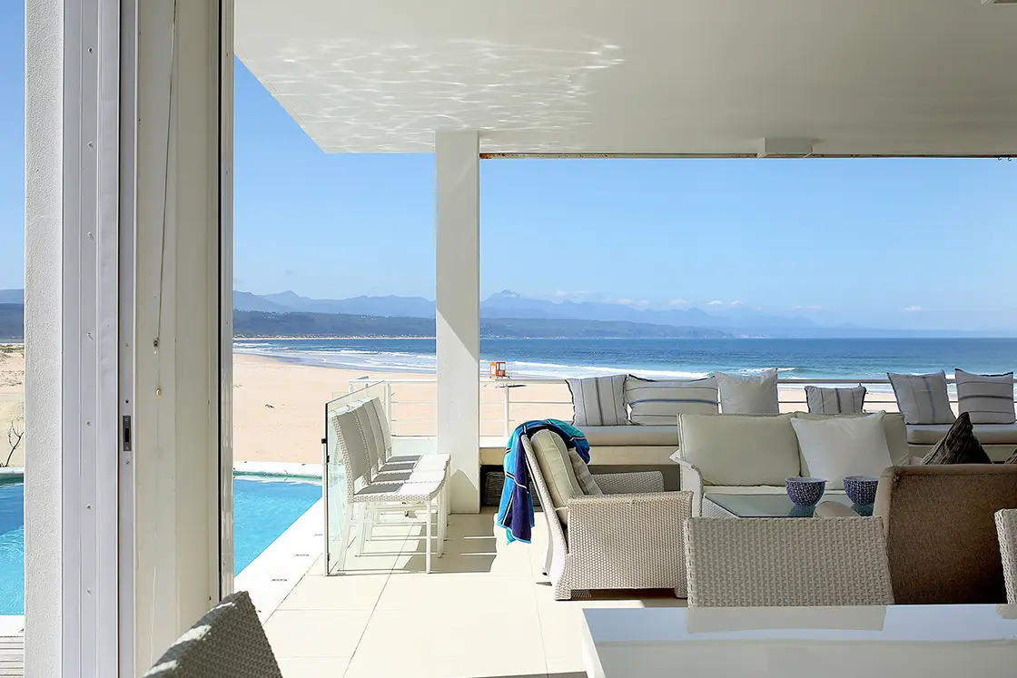 Perfect Hideaways real estate property: A living area with large sliding doors leading to a shaded outdoor patio, and a pool. Beach views. Roga Rock, Plettenberg Bay.