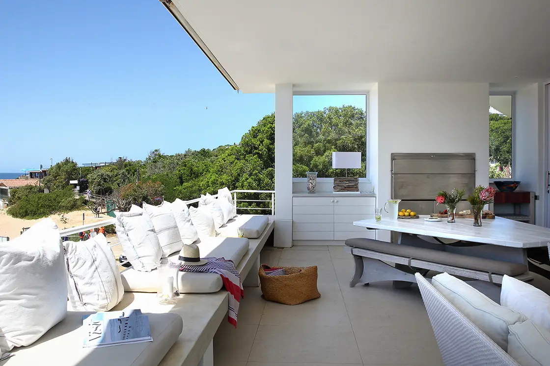 Perfect Hideaways real estate property: The balcony of a white beach house, featuring booth seating, a geometric outdoor table and fireplace, contemporary decor styling. Roga Rock, Plettenberg Bay.