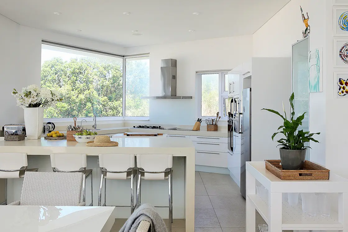 Perfect Hideaways real estate property: A kitchen area, featuring a central island with bar stools, and a contemporary kitchen style. A striking contrast between white interiors and bright decor is present throughout the home. Roga Rock, Plettenberg Bay.