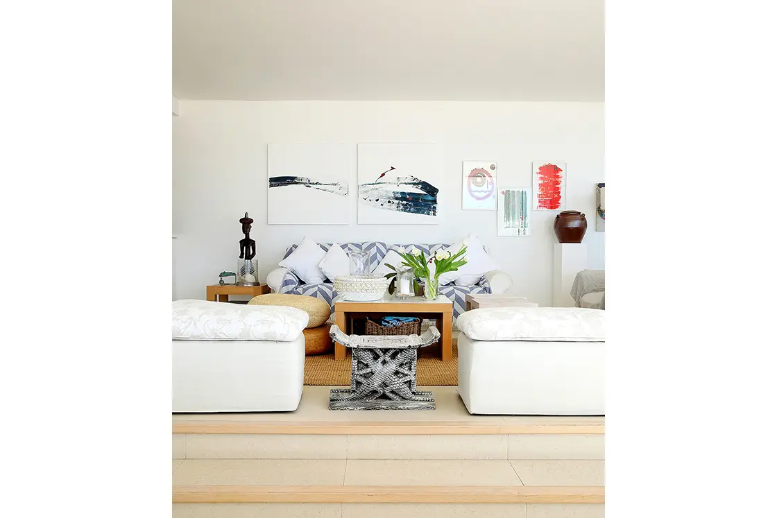 Perfect Hideaways real estate property: A living area with rustic furnishings and bright art pieces on the walls, creating a contrast to the white walls, ceilings, and couches. Roga Rock, Plettenberg Bay.