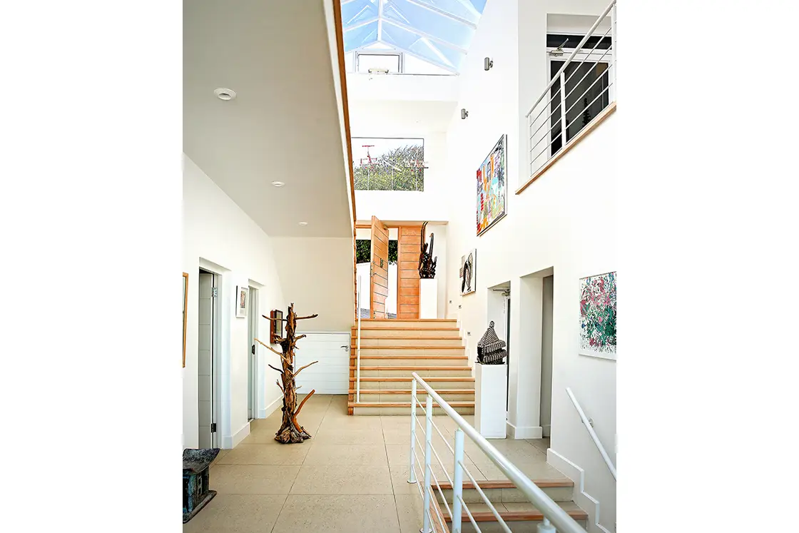 Perfect Hideaways real estate property: The entrance hall to the white beach house, featuring colourful wall art, and a large panelled window arch which allows light into the home. Roga Rock, Plettenberg Bay.