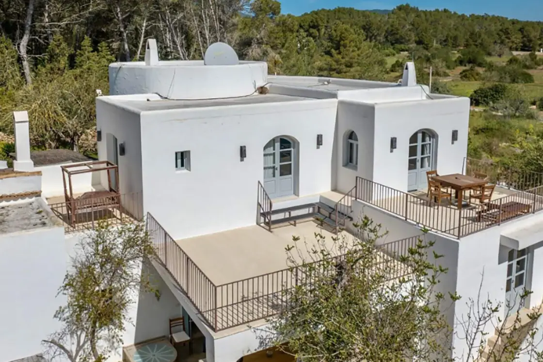 Perfect Hideaways real estate property: A stylish Finca home with white exterior walls, multiple balconies, and charming Spanish architecture. Rural countryside is visible in the background. Ibiza, Ibizan Finca.