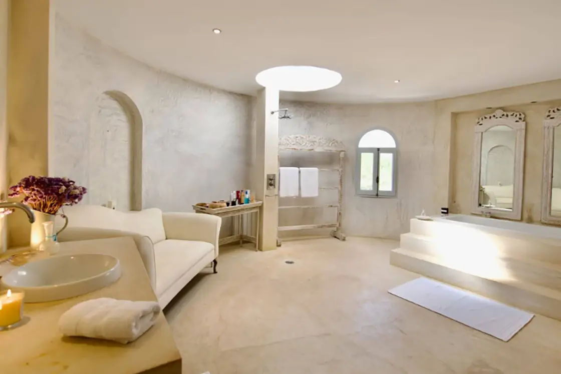 Perfect Hideaways real estate property: A luxurious bathroom area with steps leading to a bathtub, a stone basin unit, and ornate vanity mirrors. Limewash walls, and floors complete the grandiose image. Ibiza, Ibizan Finca.